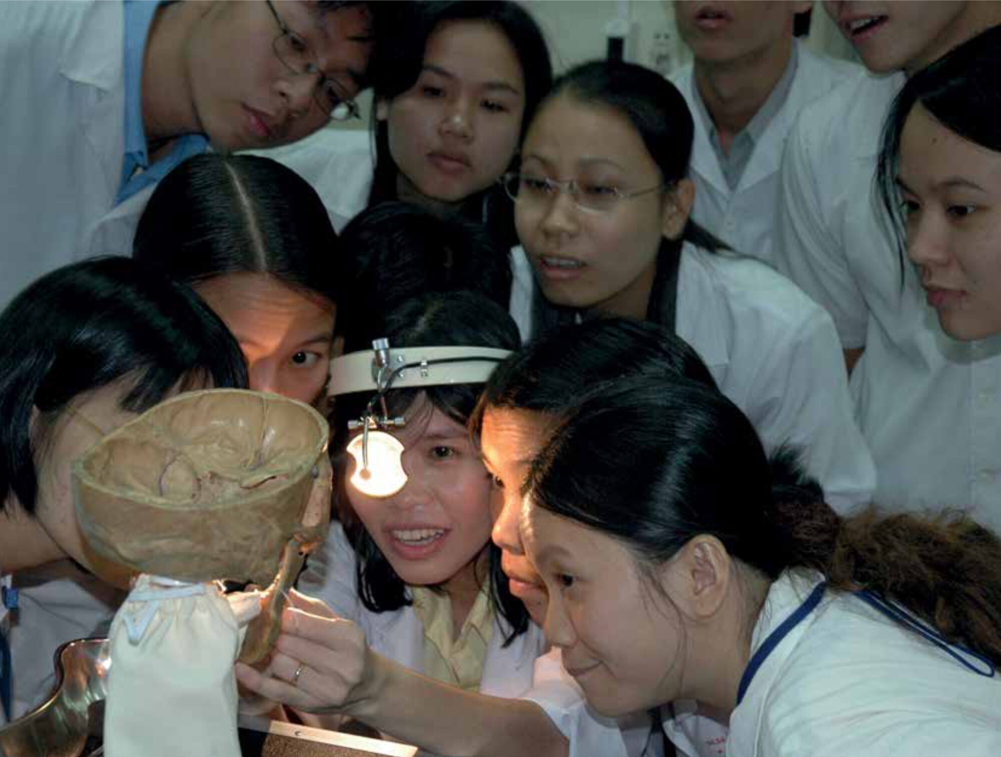 Vietnamese skills teacher using a self-made ENT model to demonstrate the examination of mouth and throat, before pairs of students practice on each other.